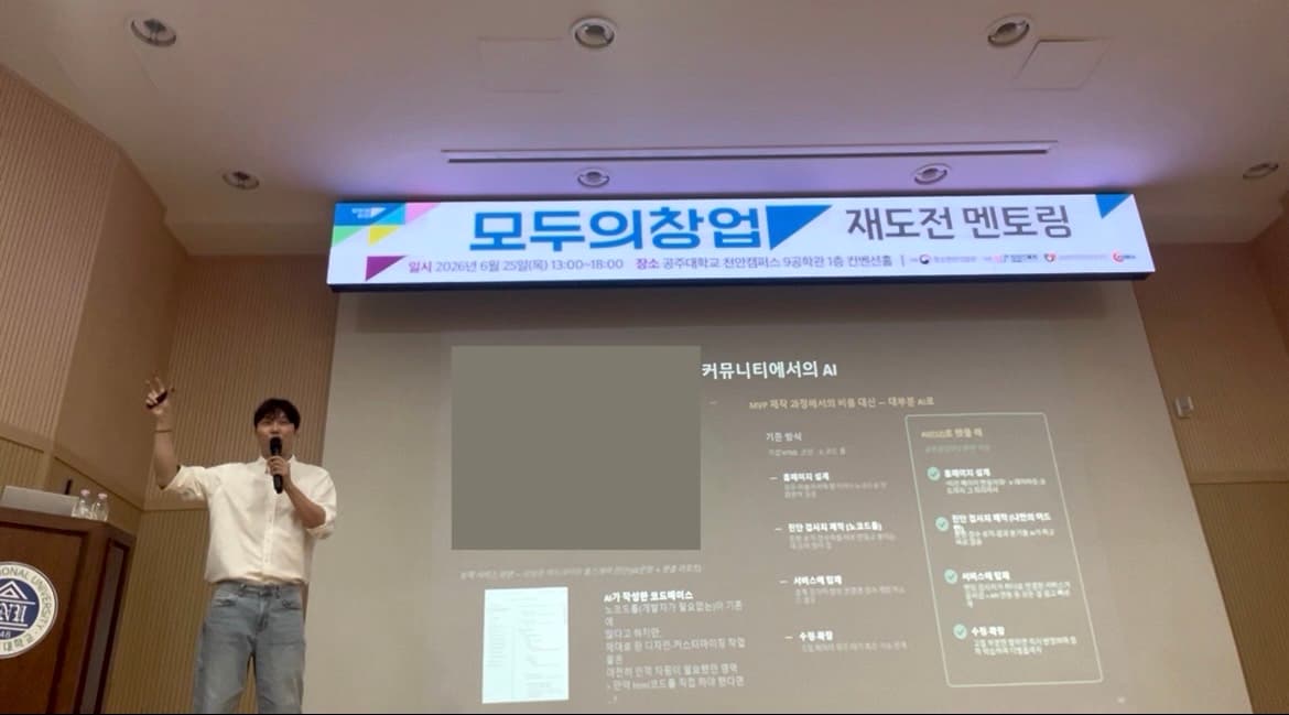 '모두의창업 재도전 멘토링' 현수막 아래 스크린 옆에서 마이크를 들고 손을 들어 설명 중인 송건호